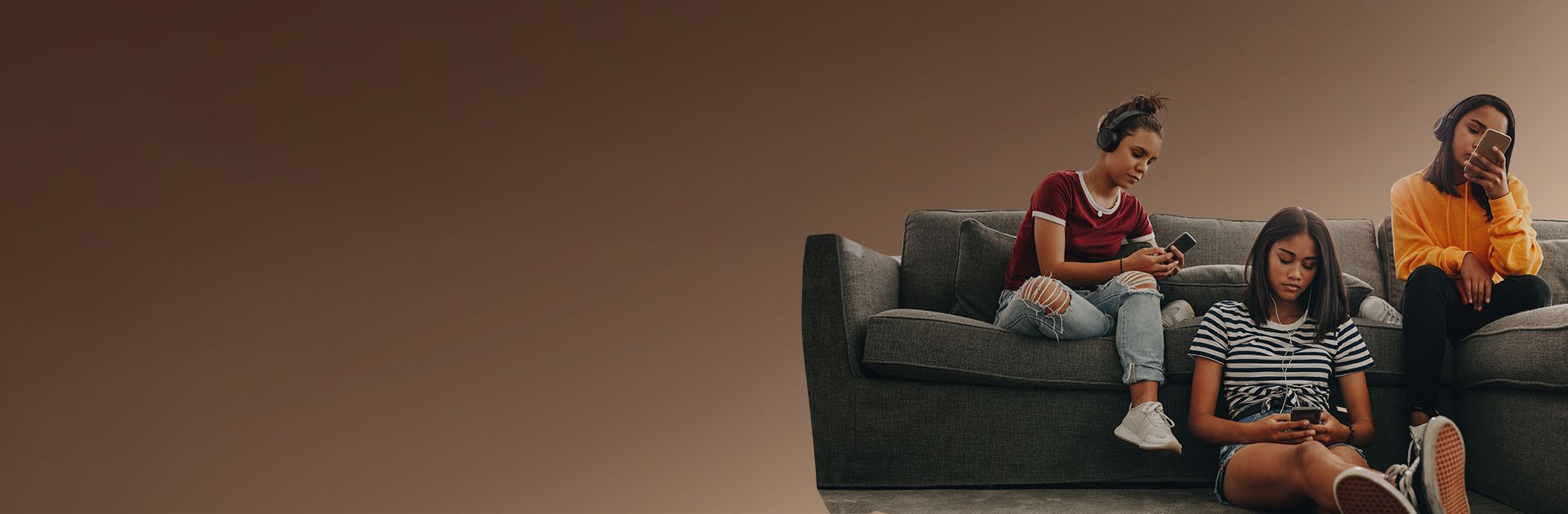 Three teenagers relaxing on a sofa with their phones and headphones